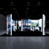 Front view of an illuminated PIXLIP GO exhibition booth showcasing vibrant panoramic cityscapes and natural landscapes, integrated with high-end bathroom interiors. The setup includes a black floor that enhances the visuals.